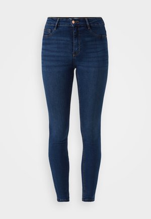 Tamno plave slim-fit traperice s visokim strukom, pet džepova i detaljima od bakra; glatka denim tekstura s blagim izbljedjivanjem.