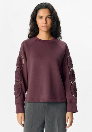 Bordeauxfarbener Pullover mit strukturierten floralem Akzent an den Ärmeln, mit Rundhalsausschnitt und gerippten Bündchen. Glattes Material, lockere Passform.