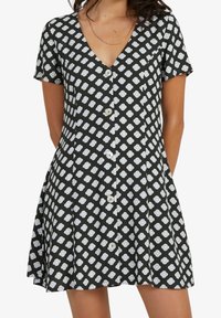 Robe noire à manches courtes avec un col en V, présentant un motif floral blanc, une fermeture à boutons sur le devant et un ourlet évasé. Texture du tissu douce.