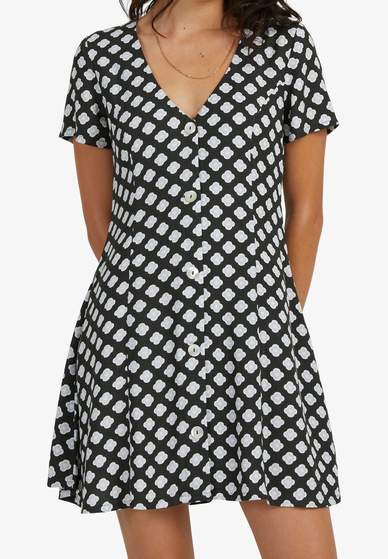 Robe noire à manches courtes avec un col en V, présentant un motif floral blanc, une fermeture à boutons sur le devant et un ourlet évasé. Texture du tissu douce.