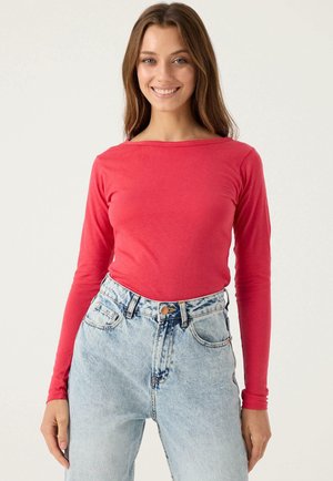 Top rojo de manga larga hecho de tela suave, combinado con jeans de mezclilla azul claro de cintura alta. Diseño ajustado con escote redondo, textura suave.