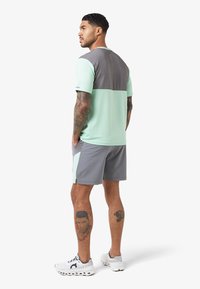 Atletische set met een mintgroen en grijs kleurblokontwerp. Het korte mouwen shirt en de shorts zijn gemaakt van lichte stof.