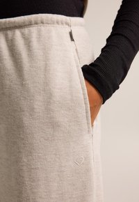 Light gray ribbed sweatpants with side pockets, featuring a subtle logo detail and an elastic waistband, paired with a black long-sleeve shirt.