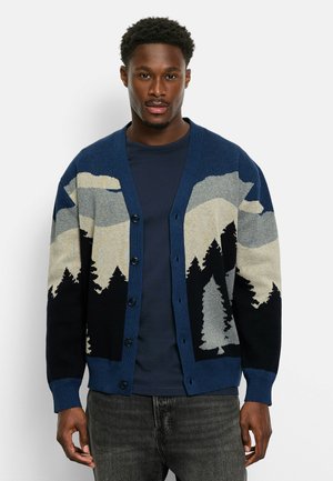 Marineblauer Cardigan mit einem Muster aus Bergen und Wald in Grau, Creme und Schwarz. Er hat einen entspannten Schnitt, einen V-Ausschnitt und eine knopfverschluss.