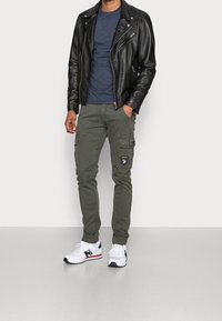 Svart läderjacka över en blå t-shirt, kombinerad med olivgröna cargobyxor med sidofickor och mörka detaljer. Vita sneakers fulländar looken.