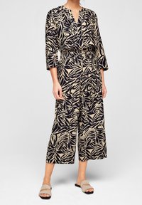 Byxdress med blommönster, v-ringning, 3/4-ärmar, elastisk midja och vida, korta ben. Färgerna inkluderar beige och svart.