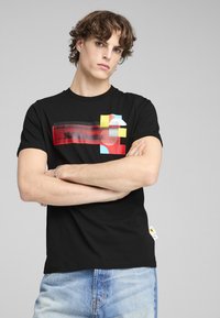 Sort bomulds t-shirt med et farverigt grafisk design med røde, gule og blå elementer. Korte ærmer og lige kant.
