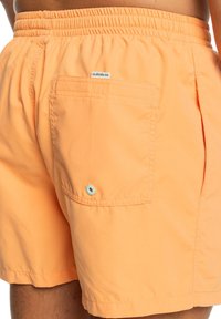 Oranje zwembroek gemaakt van lichtgewicht stof, met een elastische tailleband, achterzak met een blauwe oogjes en een zachte textuur.