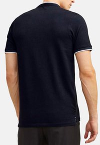Zwart polo shirt met korte mouwen, ribgebreide kraag en manchetten met witte accenten. Zacht stof, getailleerd ontwerp en een label aan de onderkant aan de linkerkant.