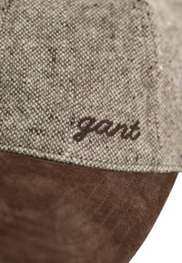 Brown fabric cap with textured beige upper, featuring embroidered "gant" logo in dark brown. Soft suede bill adds contrast.