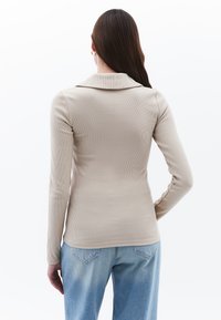 Beige geribbelde top met lange mouwen en een opgerolde kraag, aansluitend ontwerp en een gladde textuur, gecombineerd met lichtblauwe denim jeans.