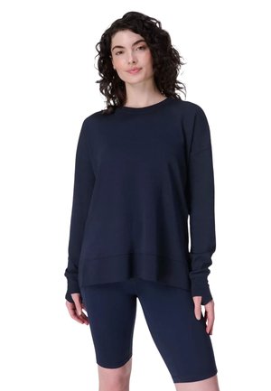 Marineblauwe sweatshirt met lange mouwen en afgezakte schouders, gecombineerd met marineblauwe fietsshorts. Zachte stof, losse pasvorm en geribbelde boorden.