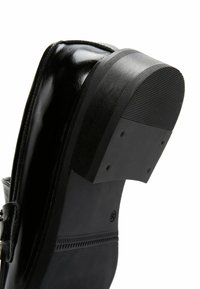 Black leather shoe with a glossy finish, featuring a thick, textured black rubber sole and square heel, showcasing its sturdy design.