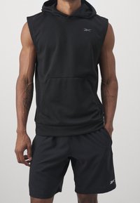 Svart ärmlös huvtröja med framficka och huva, kombinerad med matchande shorts. Tillverkad av mjukt, elastiskt material. Har subtil logodetalj.