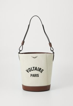 Borsa a secchiello in tela crema con base e dettagli in pelle marrone. Presenta il testo nero "VOLTAIRE PARIS" e un emblema in metallo. Spallaccio in pelle regolabile.