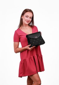 Černá syntetická taška s kulatým klopou, zdobená mnohobarevnými tečkami. Obsahuje růžové logo. Modelka má na sobě růžové šaty s volánkovým lemem.