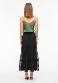 Zwarte gelaagde maxi rok met een doorschijnende overlay van stippen, gecombineerd met een groene satijnen top. De rok heeft een gerimpelde zoom en een elastische tailleband.