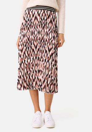 Ein knielanger Rock mit einem cremefarbenen, rosa und schwarzen Ikat-Muster, ausgestattet mit einem schwarzen elastischen Bund, kombiniert mit weißen Turnschuhen.