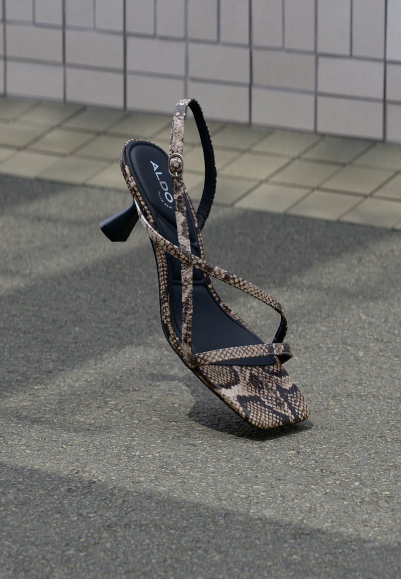 Sandalo con tacco alto stampa rettile marrone, design con cinturino incrociato, punta quadrata e soletta nera strutturata. Logo del marchio visibile sulla soletta.