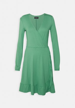 Vestido verde de manga longa em tecido leve, com um hem curto e detalhe de franzido lateral. Textura suave e design casual.
