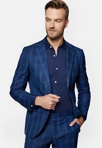 Niebieski marynarka w kratę w fasonie dopasowanym, w połączeniu z granatową koszulą zapinaną na guziki. Posiada klasyczne klapy z uzębieniem i guziki jako akcenty.