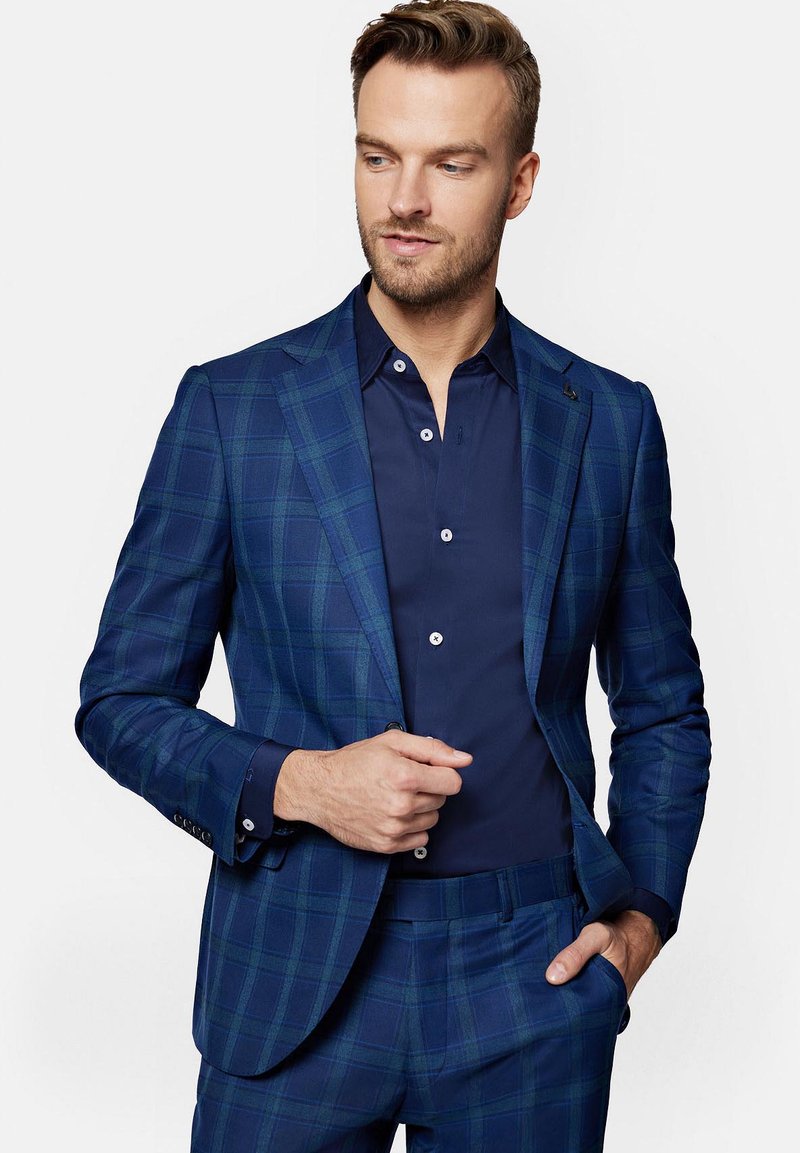 Niebieski marynarka w kratę w fasonie dopasowanym, w połączeniu z granatową koszulą zapinaną na guziki. Posiada klasyczne klapy z uzębieniem i guziki jako akcenty.