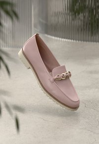 Απαλή ροζ λοφάκι με μπεζ σόλα και χρυσή διακοσμημένη ζώνη, εκτεθειμένο σε ένα ουδέτερο υπόβαθρο από ραγισμένο σκυρόδεμα.