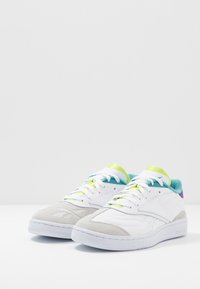 Vita sportskor i vitt med grå mockadetaljer, turkos inredning och livfulla gröna och lila detaljer. Dämpad design med strukturerad sula.