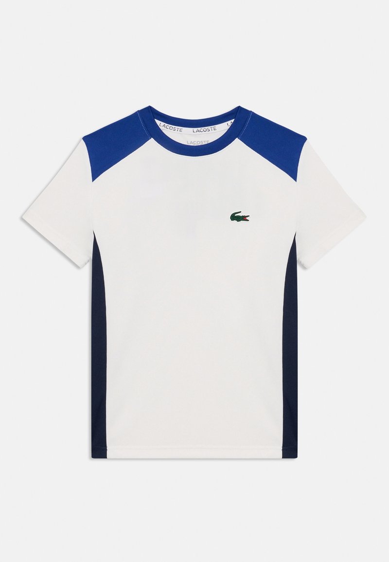 Camiseta blanca de manga corta con paneles azules en los hombros y franjas laterales, con un pequeño logo de un cocodrilo verde en el pecho izquierdo.