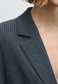 Zwarte blazer met krijtstreep, voorzien van een reverskraag en een getextureerde stof. Opvallende zilveren draadaccenten verfraaien het ontwerp.