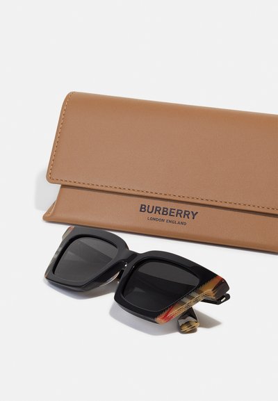 Black square sunglasses with textured accents, alongside a tan leather case embossed with "Burberry London England."