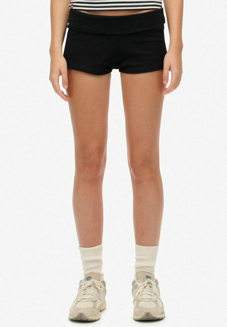 Shorts deportivos negros con una cinturilla ancha, combinados con zapatillas beige y calcetas blancas. Material suave, diseño ajustado, estilo minimalista.