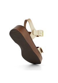 Platform sandalen met een crèmekleurige band en gesp, met een bruine ribbelzool. Het ontwerp heeft een lichte kromming bij de teen en de hak.