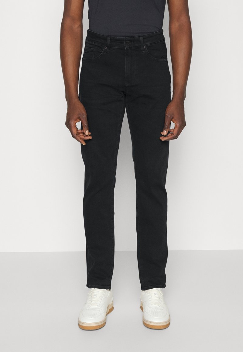 Mustat farkut slim fit -leikkauksella, viidellä taskulla ja vyölenkeillä. Yhdistetty valkoisiin lenkkareihin, joissa on teksturoitu pohja ja nauhakiinnitys.