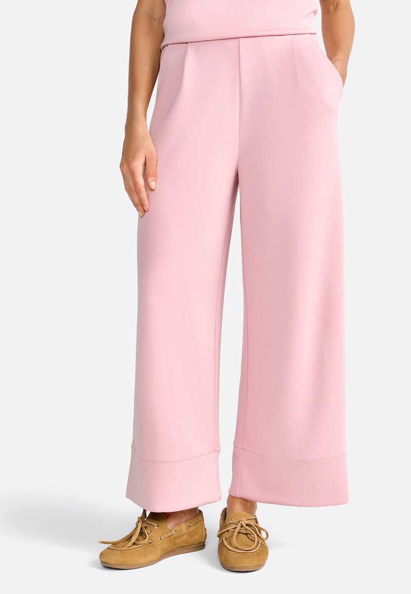 Pantaloni a gamba larga rosa realizzati in tessuto morbido, dotati di due tasche frontali e orlo ripiegato. Abbinati a scarpe con lacci color marrone chiaro.