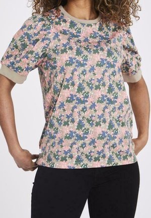 Mujer que lleva una camiseta de manga corta con estampado floral, con puños y cuello beige, combinada con pantalones negros.