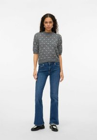 Grå tröja med korta ärmar och texturerat prickmönster, i kombination med blå utsvängda jeans och svarta skor. Enkel design, modern passform.