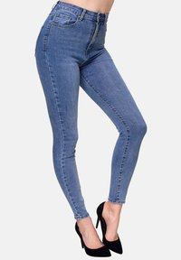 Jeans ajustados de lavado medio, diseño de cintura alta, costuras en contraste y estilo de cinco bolsillos, combinados con zapatos de tacón negro.