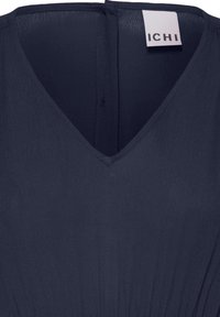 Robe bleu marine à col en V avec tissu texturé et fermeture éclair visible dans le dos, dotée d'une étiquette blanche portant le texte "ICHI".