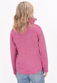 Fliisist pullover eredas roosas, kõrge kaelusega ja pikade varrukatega. Omab tekstuurset mustrit ning ümarat hemii taga.