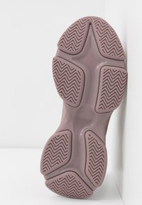 Semelle d'une basket mauve avec des motifs de bande de roulement en zigzag sur cinq sections de grip en caoutchouc sur fond blanc.