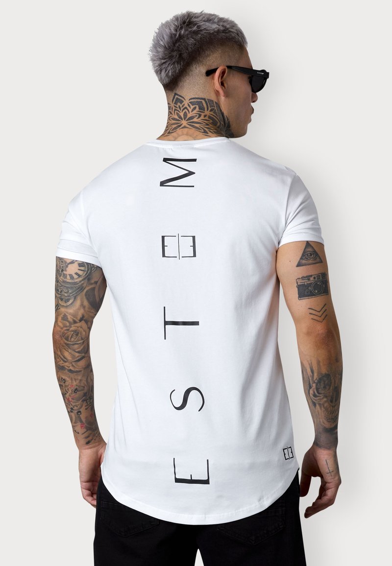 White short-sleeve T-shirt featuring bold black vertical text on the back, round neck, and a curved hem. Displays tattoos on the arm.