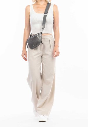 Kobieta ubrana w biały prążkowany crop top, beżowe spodnie o szerokich nogawkach, białe trampki oraz czarną skórzaną torbę na ramię z szerokim paskiem.
