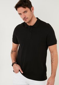 Polo negro de rayas con cuello y tapeta de tres botones. Manga corta y corte ajustado. Diseño sencillo sin patrones ni acentos.