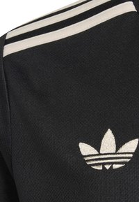 Zwarte sportshirt van textuurstof, met drie horizontale witte strepen op de schouder en een wit geborduurd logo.