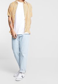 Camicia a maniche corte gialla a righe sopra una t-shirt bianca; jeans baggy azzurri chiari; sneakers bianche. Design minimalista con vestibilità casual.