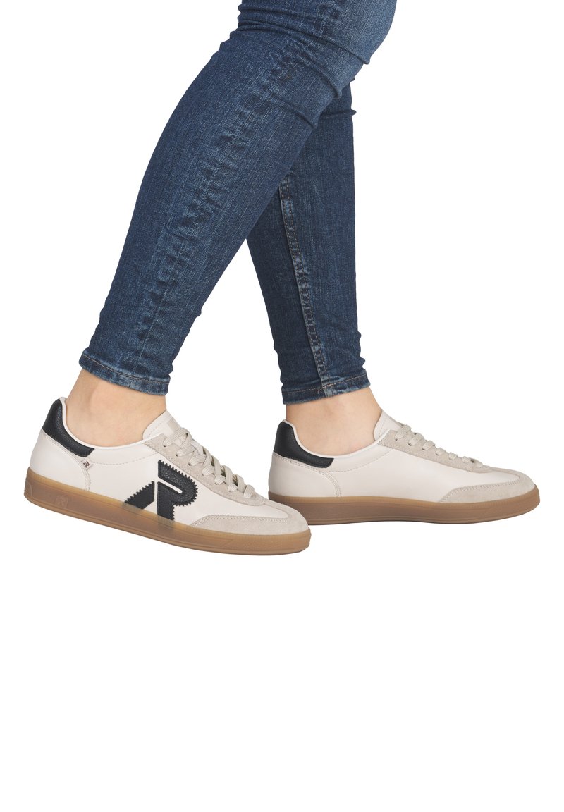 Baskets en cuir beige avec des accents noirs, design à lacets et semelle en caoutchouc texturé. Présente un logo noir bien visible sur le côté.