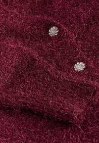 Tissu texturé bordeaux avec deux boutons ronds en strass brillants intégrés dans un rabat de poche.