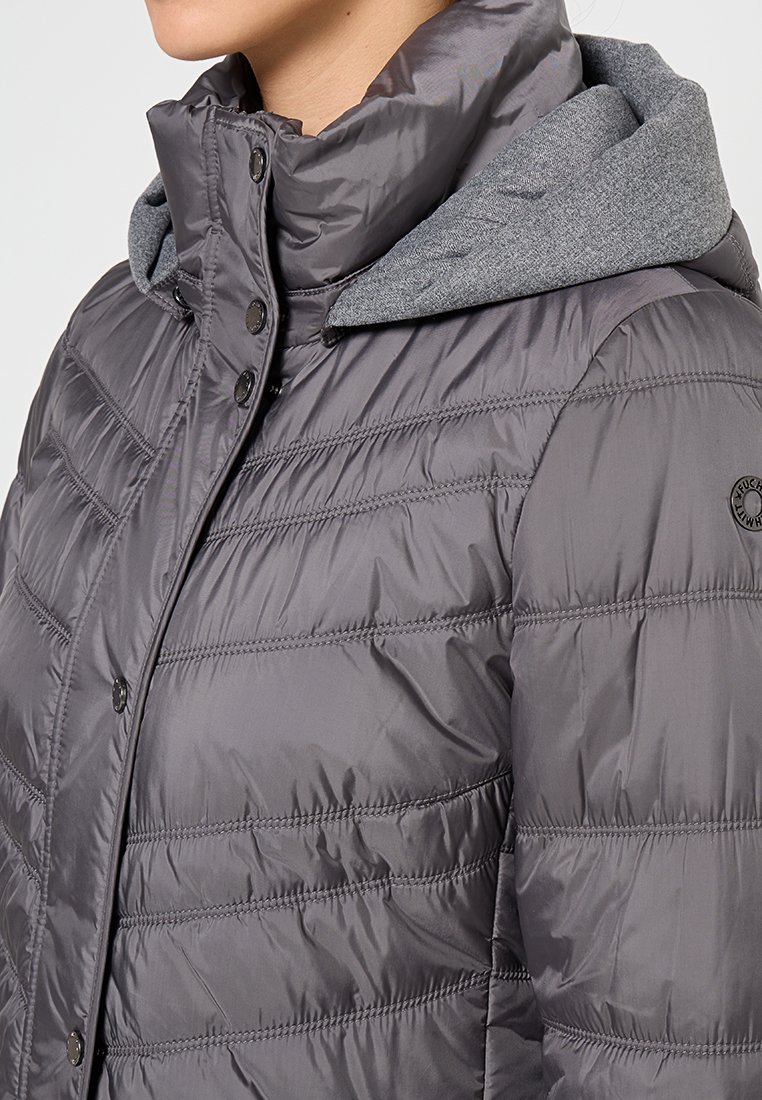 Kobieta w szarej pikowanej kurtce z zatrzaskami i kontrastującym dzianinowym kapturem, prezentująca górną część tułowia i okolice szyi.