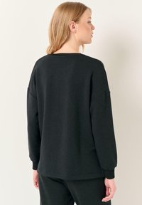 Felpa nera con vestibilità rilassata, caratterizzata da maniche lunghe, polsini a coste e scollo rotondo. Texture morbida e design semplice.